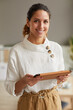 © Seventyfour - Vertical waist up portrait of smiling successful businesswoman looking at camera and holding digital tablet while working from home or in office