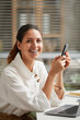 © Seventyfour - Vertical portrait of smiling elegant woman looking at camera and holding smartphone while enjoying work from home