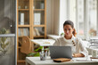 © Seventyfour - Wide angle portrait of modern businesswoman using laptop while sitting at desk by window in office, copy space