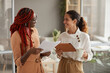© Seventyfour - Waist up portrait of two successful young businesswomen discussing documents and smiling cheerfully while standing in modern office interior, copy space