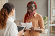 © Seventyfour - Waist up portrait of young African-American businesswoman talking to female manager and smiling cheerfully while standing in modern office interior