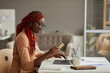 © Seventyfour - Side view portrait of young African-American woman holding credit card while enjoying online shopping at home office, copy space