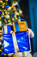 Three Boxes In Wrapping Shiny Paper In Children's Hands On The Background Of A Christmas Tree