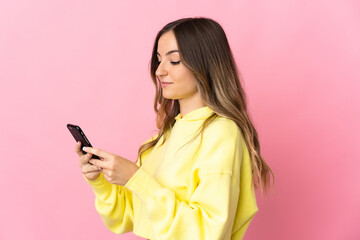 Young Romanian woman isolated on pink background sending a message or email with the mobile