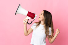 Young Romanian Woman Isolated On Pink Background Shouting Through A Megaphone To Announce Something In Lateral Position