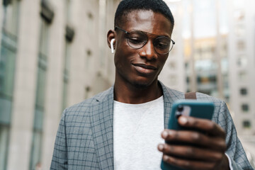 Wall Mural - Pleased african american man in earphones using mobile phone