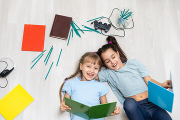 family, leisure and childhood concept - happy sisters lying on floor and drawing and doing homework at home