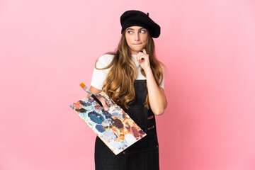 Young artist woman holding a palette isolated on pink background having doubts and thinking