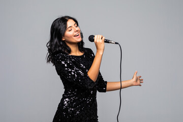 Portrait of happy young woman singing with microphone isolated on gray background