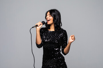 Beautiful brunette woman singing to microphone isolated on gray background