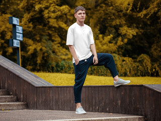 Poster - Male white t-shirt template on a guy standing on a blurred background of the park, with a hand in his pocket.