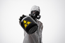 A Scientist Man In A Protective Radiation Suit And Gas Mask Holds A Large Black Jar  With Radioactive Sign In His Hands. Biological Hazard. Copy Space. Isolated Background