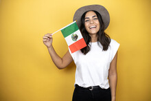 Beautiful Woman Wearing Casual White T-shirt And A Hat Standing Over Yellow Background Holding The Mexican Flag