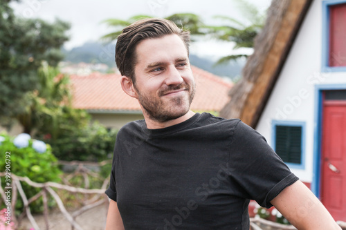 Fotomural A young man in a black t-shirt smiling and looking aside, outdoors