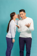 Wall Mural - Portrait of a happy young couple standing together over blue background, telling secrets