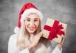 © Alen-D - Surprised beautiful blond woman with wears christmas santa claus hat - cap and holding red gift box - present with ribbon, isolated on gray background