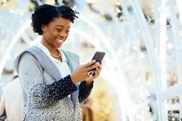 African American woman in a shopping center with a cell phone preparing for the holidays