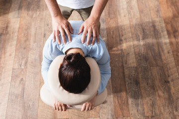 Wall Mural - Top view of masseur doing seated massage of shoulders for brunette woman on textured background