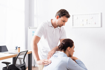 Wall Mural - Focused masseur looking at brunette woman, while doing back massage in office