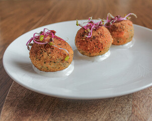 Wall Mural - Fancy croquettes over goat cheese sauce. plated on white plate over wooden table. 