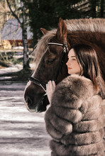 A Girl In A Beautiful Dress And Fur Coat With A Horse Stands Near The