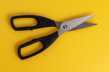 Black kitchen scissors on a yellow background.