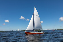 A Red Sailing Boat On The Kagerplassen With 2 People Sailing In The South-Holland Municipality Of Warmond In The Netherlands. On A Beautiful Day With A Blue Sky.
