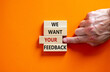 Wooden blocks with text 'we want your feedback'. Male hand. Beautiful orange background, copy space. Business concept.