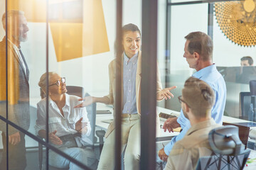 Wall Mural - Sharing fresh ideas. Young mixed race female office worker discussing something with colleagues while having a meeting in the modern office