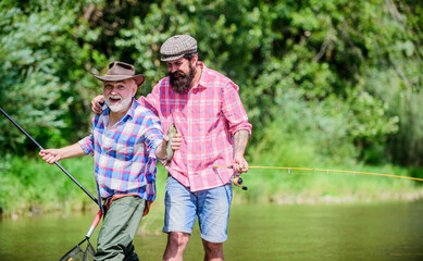 Wall Mural - Sunny summer day at river. Fisherman family. Hobby sport. Fishing peaceful activity. Father and son fishing. Rod tackle. Fishing equipment. Grandpa and mature man friends. Fishing with spinning reel