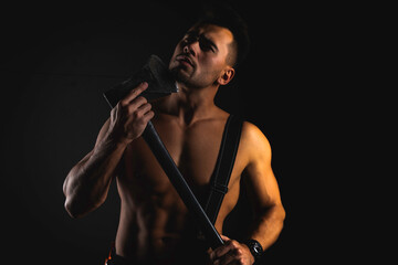 Wall Mural - young handsome adult, muscular firefighter in uniform holding ax fire equipment in hands, pensive, isolated on dark background. Low key