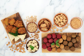 Healthy plant based food for a vegan diet with a variety of tofu balls & sausages, onion bhajis, samosas, soy beans, tvp & bean curd. Ethical eating concept. Flat lay on marble.
