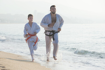 Positive man and boy in karate uniform doing exercises at sunny seaside