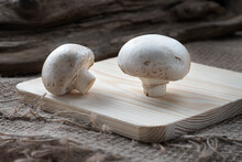 Closeup Of Raw Whole Large Royal Mushrooms On Wooden Cutting Board, Natural Sackcloth And Piese Of Wood Background. Artificially Grown Champignons. Vegetarian Food. Selective Focus
