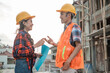 © Odua Images - Asian male and female contractors discuss with hand gestures wearing safety helmets with the background of the unfinished building