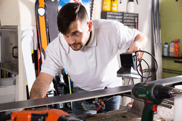 Confident diligent smiling master of ski service professionally performing sharpening of edges on skis