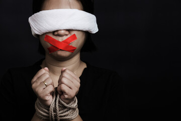 Wall Mural - Slave Asian woman blindfold wrapping mouth with red adhesive tape, tied with chains and closed her eyes black background. Freedom speech censorship and stop talk, International Human Rights day