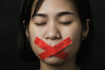 Wall Mural - Asian woman blindfold wrapping mouth with red adhesive tape on black background. Freedom speech censorship and stop talk, International Human Right day