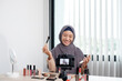 © Orathai - Muslim women making video beauty vlogger bloggers doing a cosmetic makeup tutorial vlog with brushes looking camera Save clips and share them on social media live via the internet Online