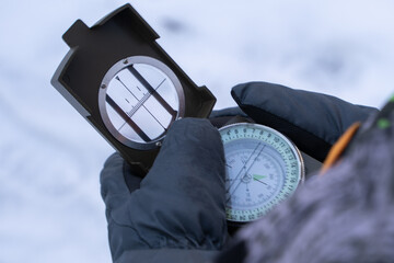 A boy in mittens in the winter forest holds a compass in his hands. Boy trying to navigate in the forest using a compass