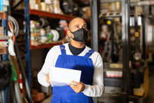 Latin American Warehouse Worker Wearing Protective Mask Making Notes During Inventory Of Building Materials. Concept Of Health Protection During Coronavirus Pandemic