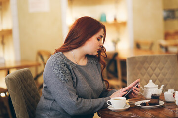 Caucasian beautiful plus size lady overweight woman drinks coffee and works. Difficult choice concept, diet or delicacy. Brunette woman with long hair in a cafe