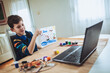 Focused boy painting and watching online course on laptop while practicing at home. Online training, online classes.