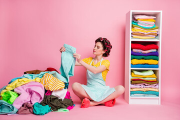 Poster - Portrait of attractive glamorous focused housemaid homemaker sitting on floor folding things isolated pink pastel color background