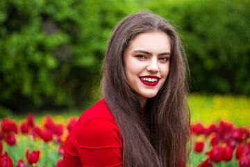 Young beautiful brunette model posing on a background of red tulips