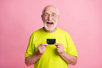 Poster - Photo of old happy excited cheerful grandfather wear lime t-shirt hold credit card isolated on pink color background