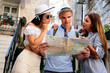 © NDABCREATIVITY - Happy traveling friends tourists sightseeing with map in hand
