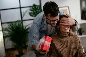 Wall Mural - Boyfriend surprising his girlfriend with a gift. Young man giving a gift box to his girlfriend.