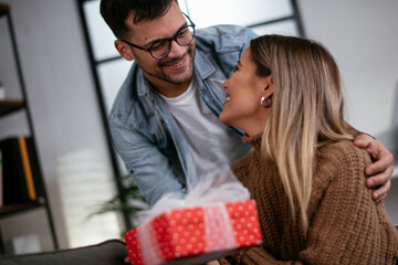 Wall Mural - Boyfriend surprising his girlfriend with a gift. Young man giving a gift box to his girlfriend.