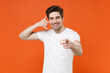 © ViDi Studio - Smiling young man in basic casual white blank empty t-shirt standing doing phone gesture like says call me back pointing index finger on camera isolated on bright orange background, studio portrait.